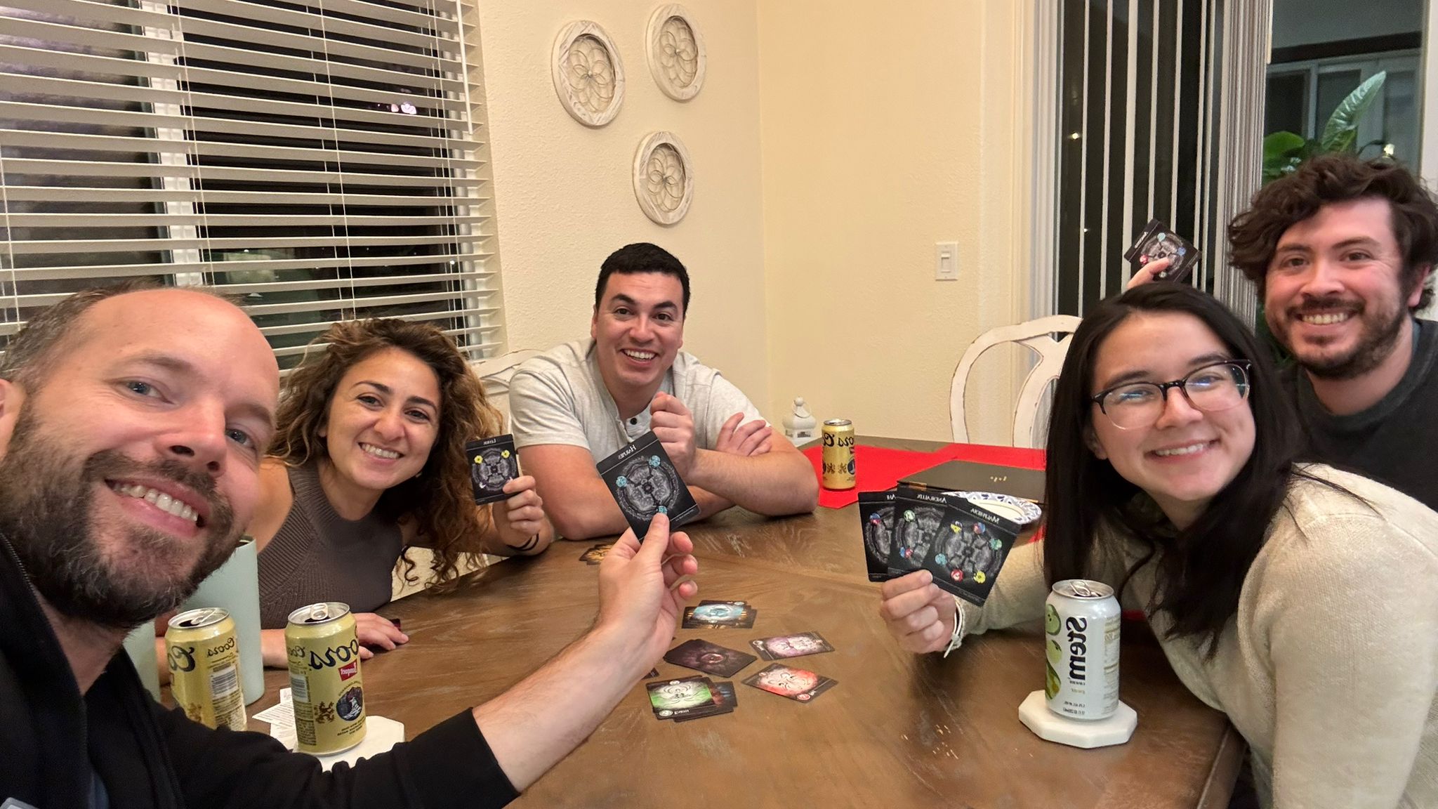 Five players around a table mid-game, grinning and holding up their Team EvL cards