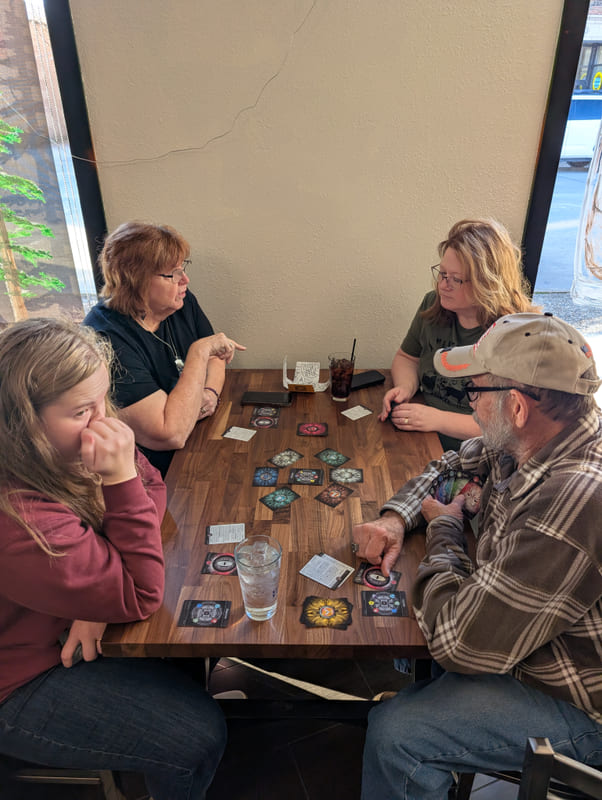 Four players in a café booth, Element tokens spread across the table